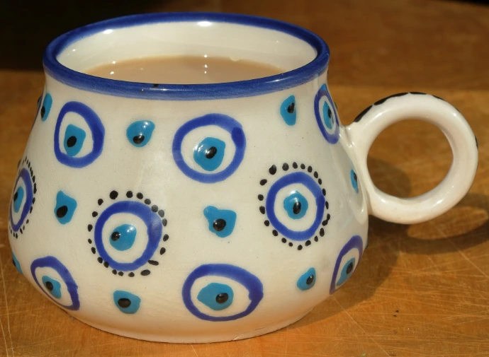 A ceramic mug with blue eye patterns filled with coffee on a wooden surface.